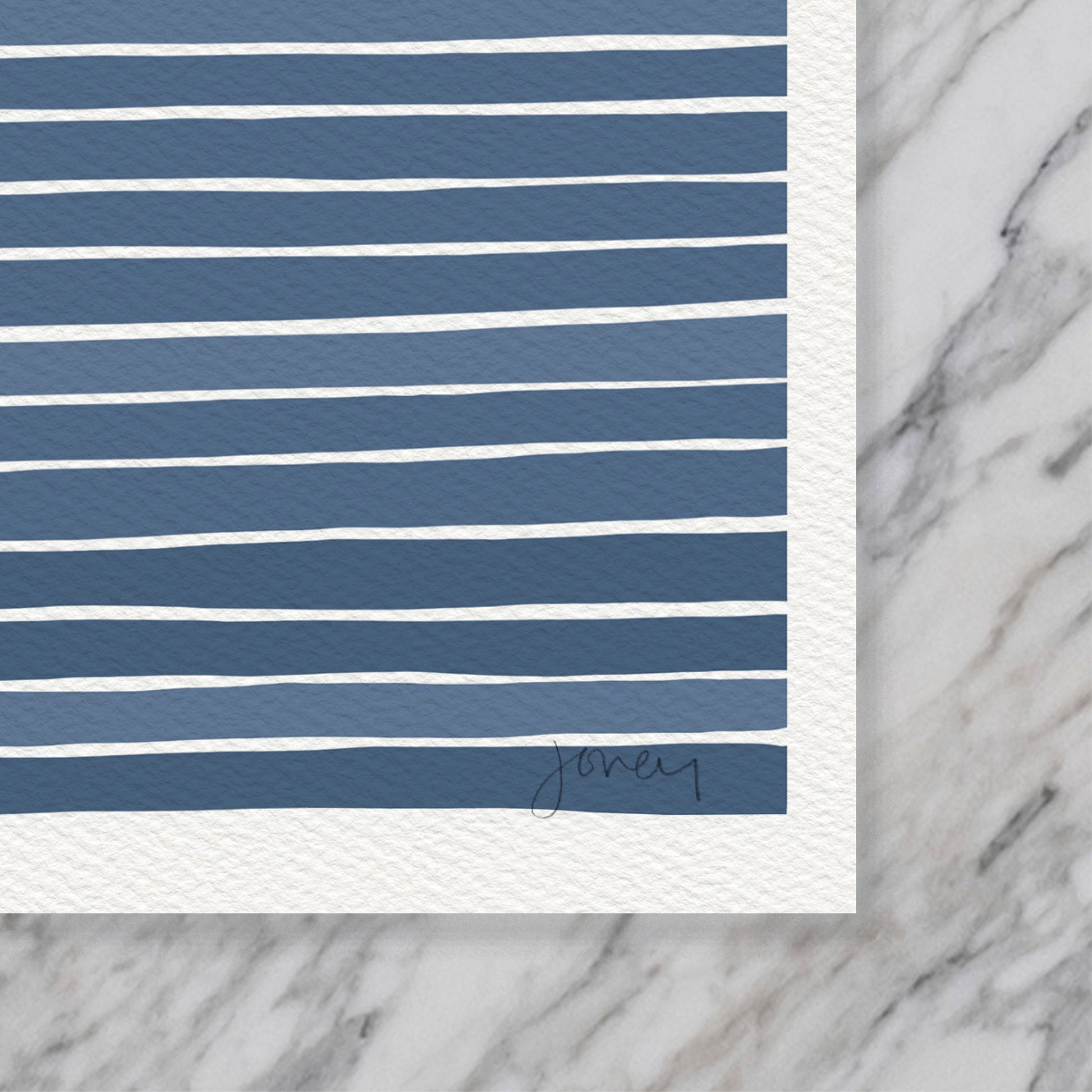 a closeup of the bottom right corner of an art print by artist Jorey Hurley. the visible section of the print shows navy blue and white stripes and the artists signature. the paper is slightly textured and very thick.