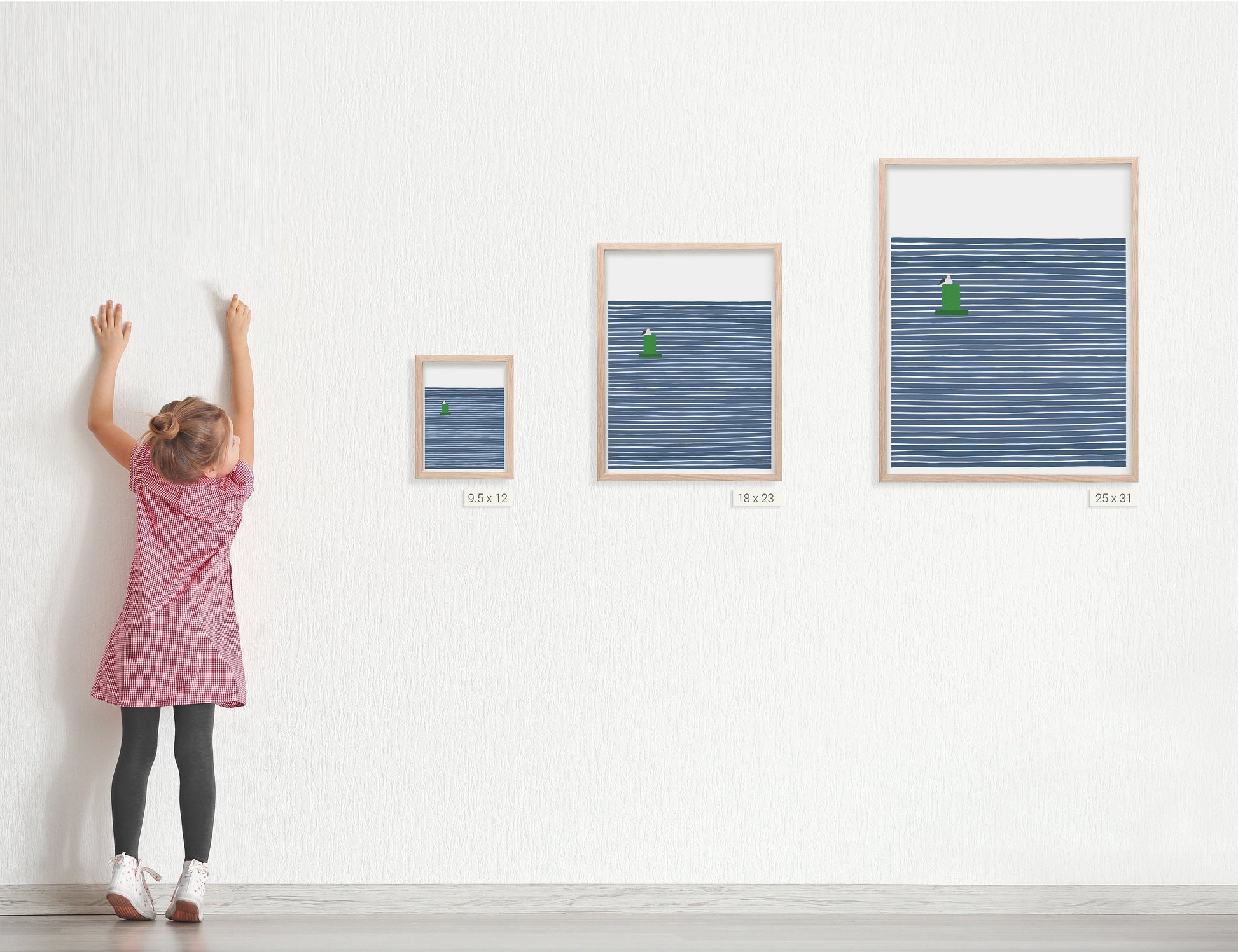 a young girl standing next to three framed art prints by artist jorey hurley. the prints are different sizes . the image on the prints is a coastal scene of a seagull sitting on a buoy with a navy blue striped background.